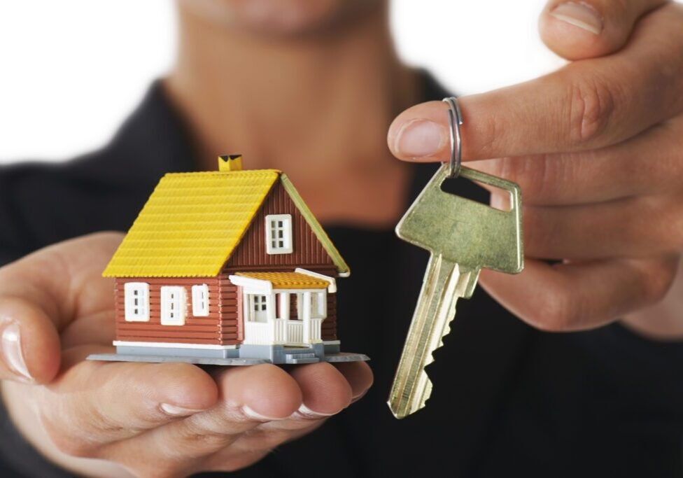 Young adult woman presenting a house in her palm and the key to it